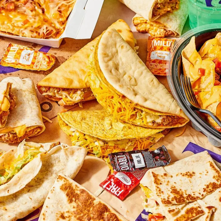 Taco Bell food spread with tacos, quesadillas, nachos, sauce packets, and drinks
